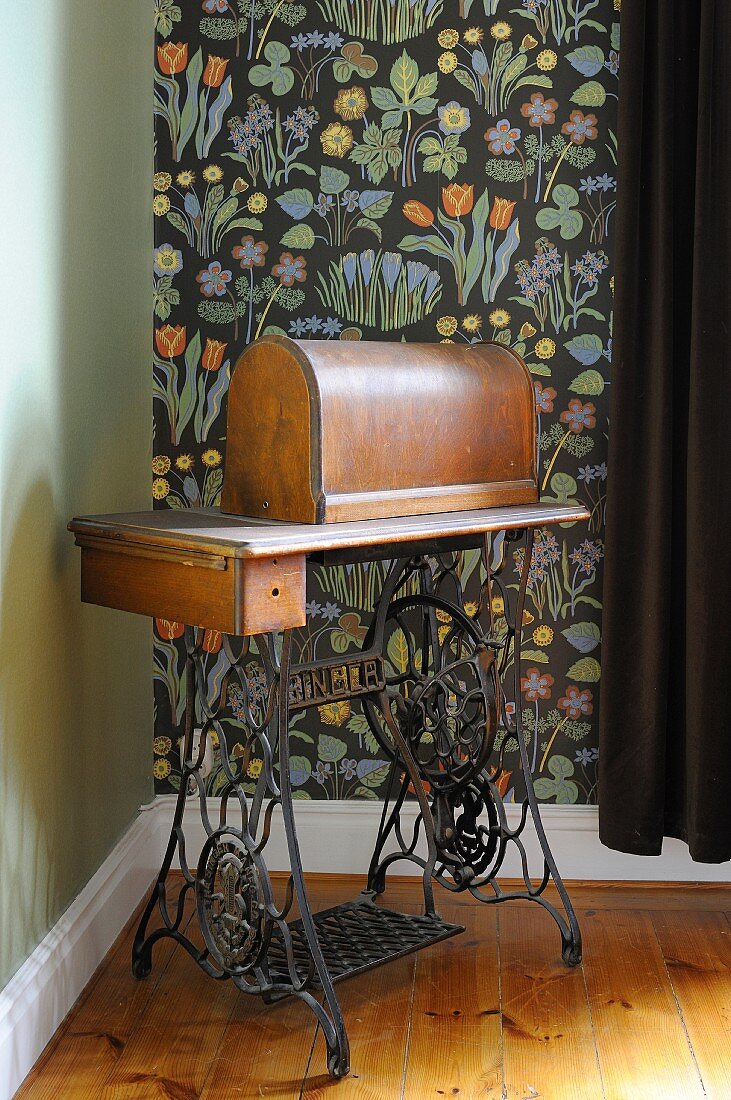 Old pedal sewing machine against floral wallpaper with black background