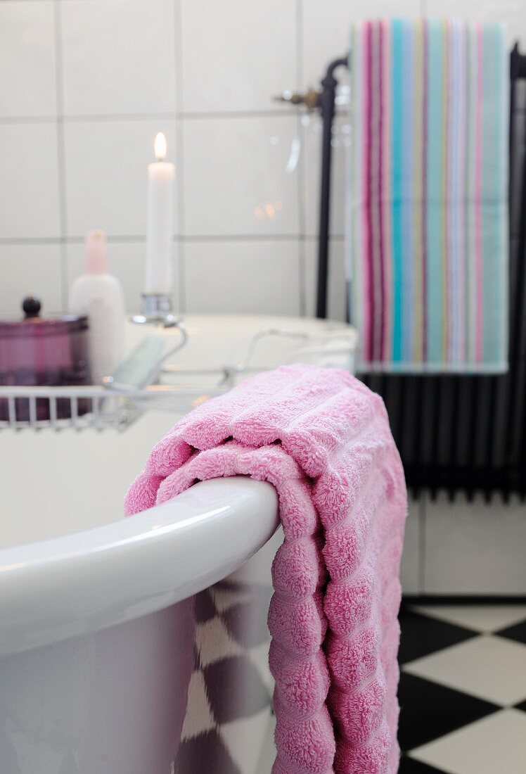 Pastellviolettes Handtuch auf freistehender Badewanne; Ablagegitter mit Kerze im Hintergrund