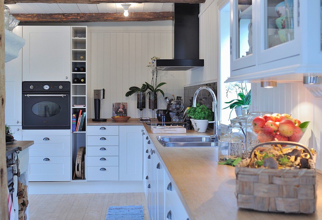 Modern, L-shaped, fitted kitchen with white cupboards and white wood-clad walls