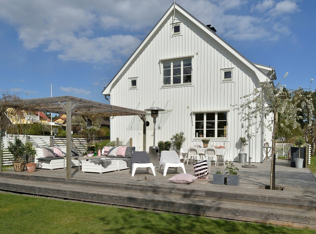 Idyllisches weißes Schwedenhaus mit großer Holzterrasse und weißen Outdoormöbeln