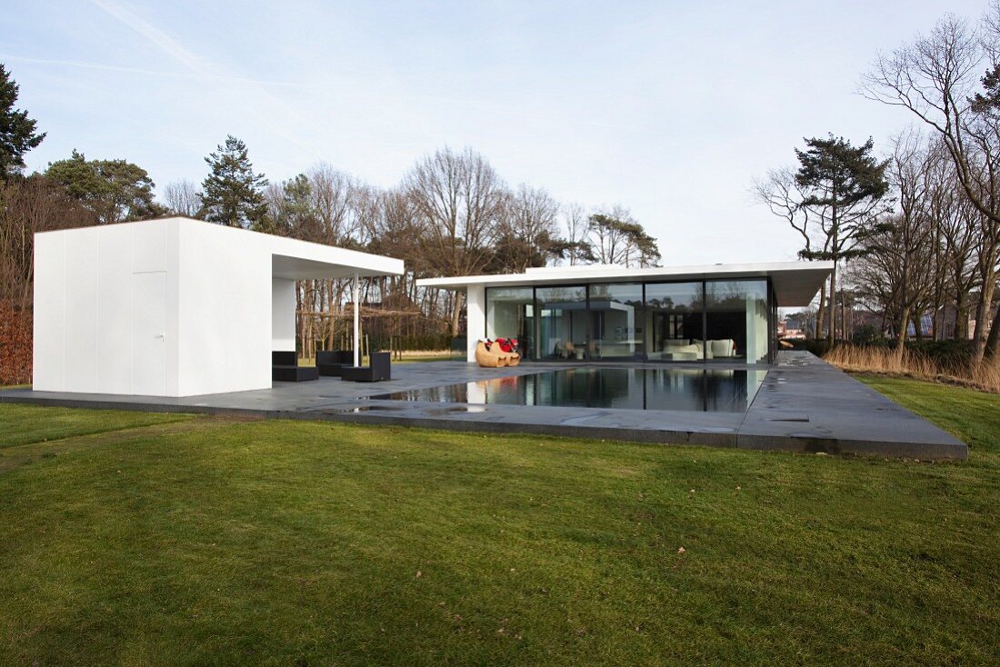 Contemporary house and summer house with roofed terrace of dark grey stone flags and pool in open landscape