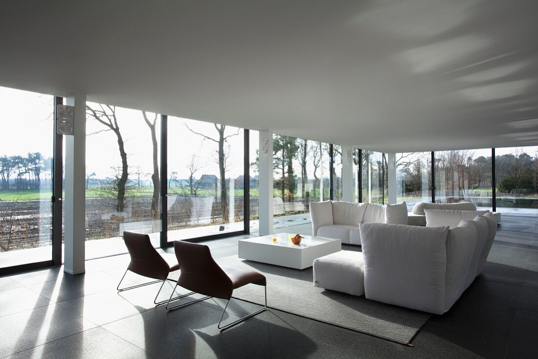 White sofa set in minimalist, elegant interior with panoramic view of autumn landscape