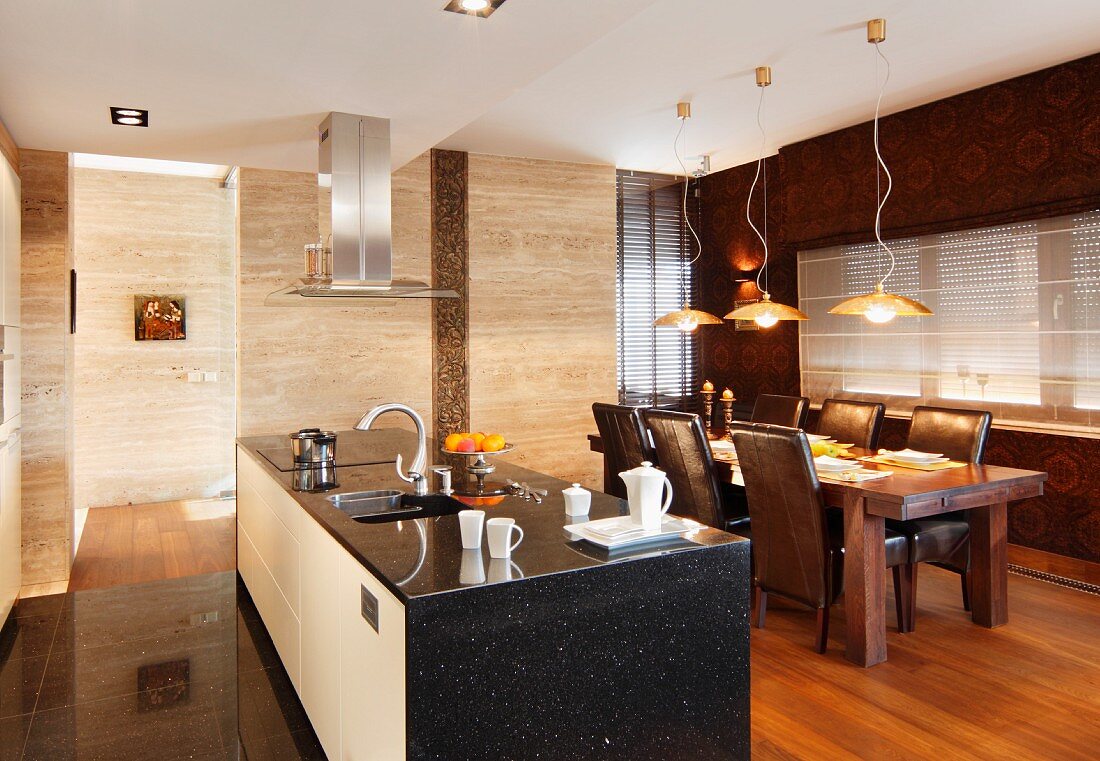 Free-standing kitchen counter clad in black stone and tasteful dining area with leather-covered chairs below modern pendant lamps