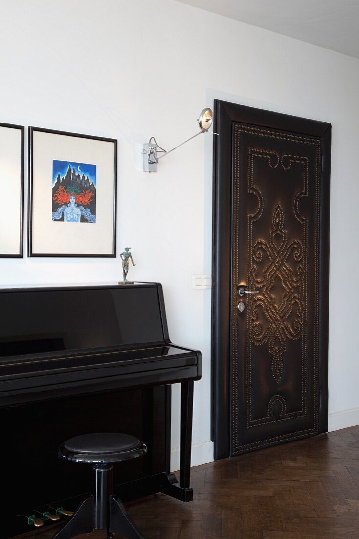 Black lacquered piano and stool next to door with leather cover and pattern of studs in traditional interior