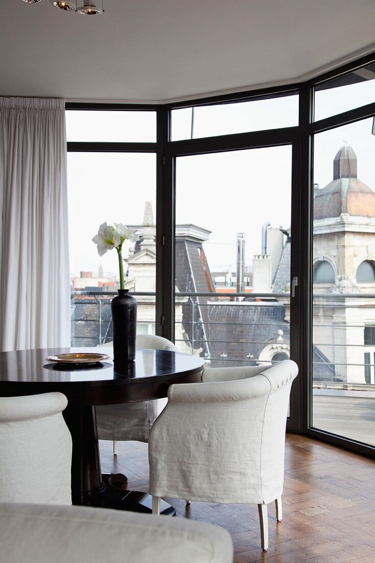 Armchairs with white loose covers in bay with floor-to-ceiling windows and view of cityscape