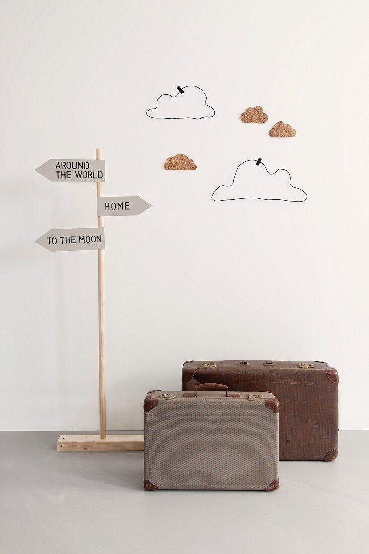 Spieldeko im Kinderzimmer mit Reisekoffern unter Wegweiserschildern und selbstgebastelte Wolken aus Draht und Pappe an der Wand