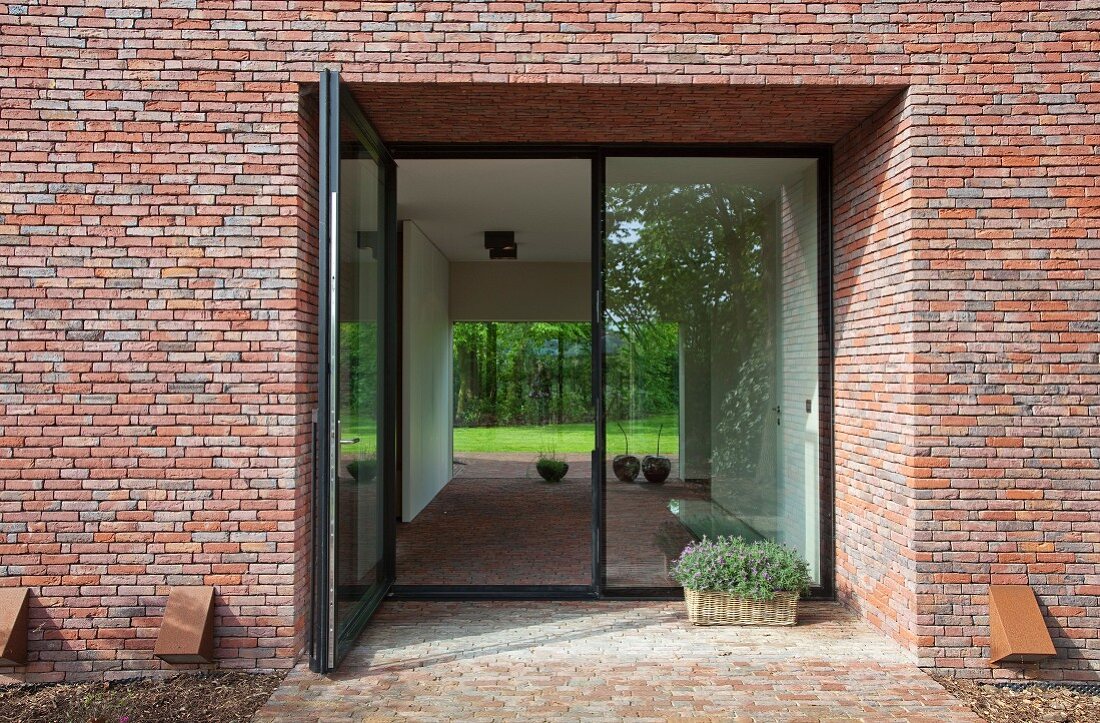 Recessed front doors in brick facade of Belgian house; view through large glass doors into garden