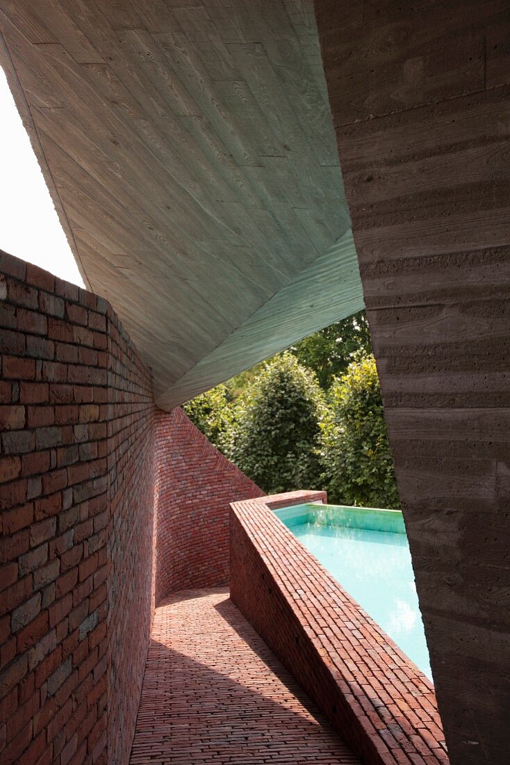 Boldly shaped concrete roof over sloping brick path next to polygonal swimming pool