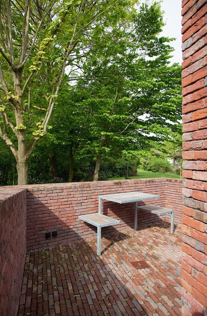Klinkerterrasse mit minimalistischer Sitzplatz-Einheit, dahinter der Garten mit altem Baumbestand im Frühling