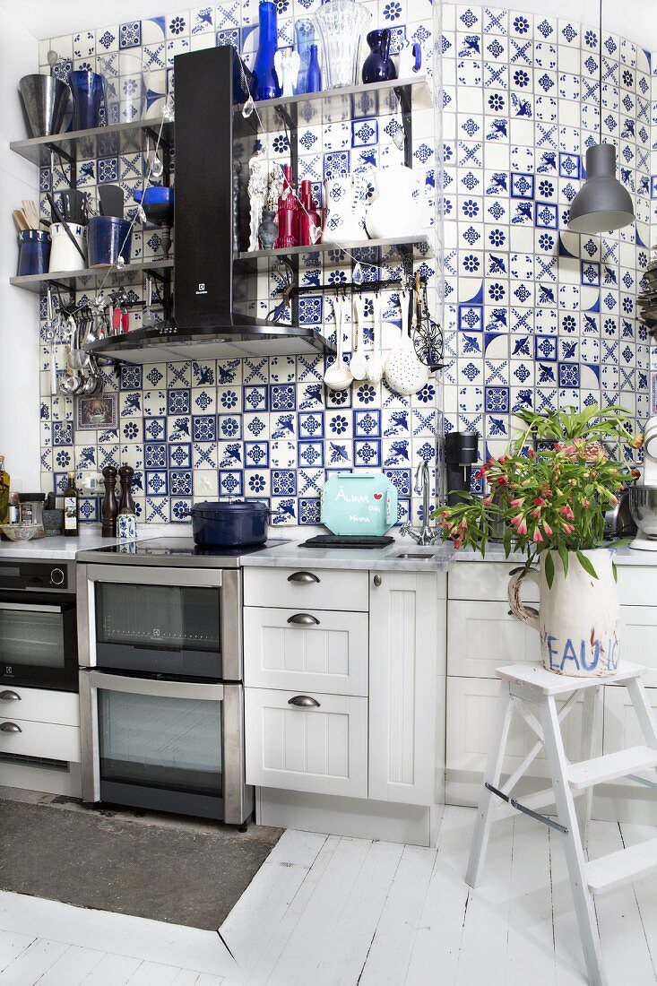 weiße Küchenzeile vor hoher gefliester Wand mit traditionellen weiss-blauen Fliesen im Landhausstil