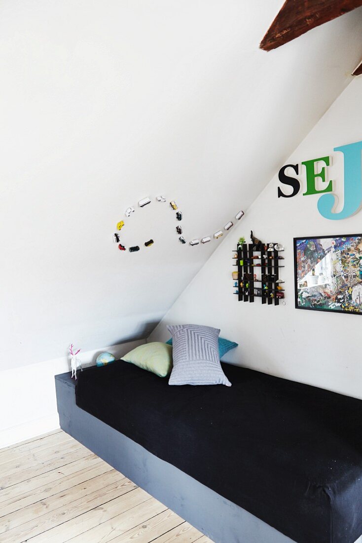 Single bed under sloping ceiling with creative arrangement of ornaments and decorative lettering on walls