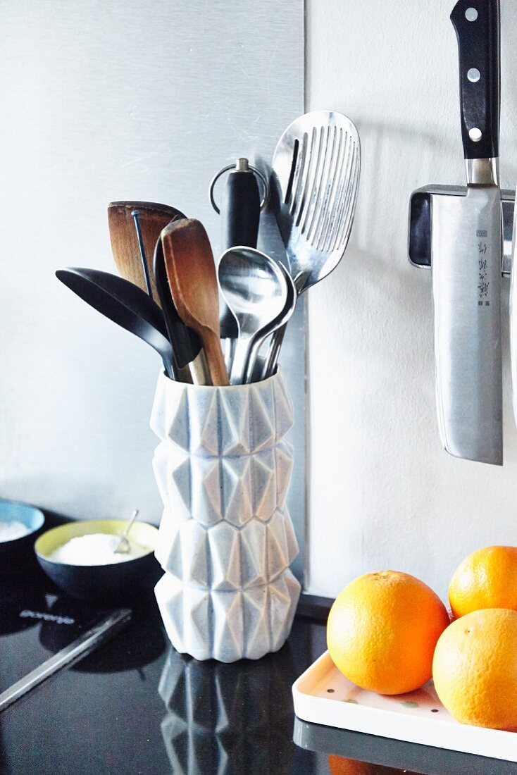 Wooden spoons and utensils in white, retro vase on black granite kitchen worksurface