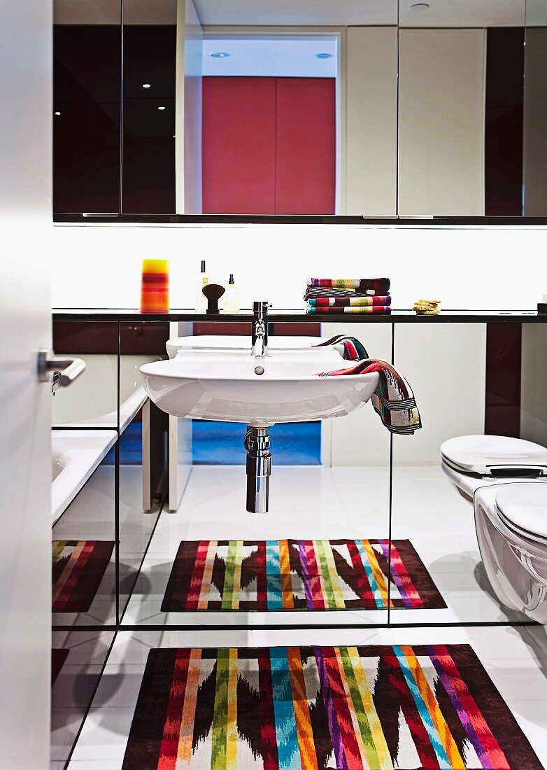Bunt gemusterter Teppich, reflektiert in verspiegelter Vormauerung mit Waschbecken und Hänge-WC, darüber Spiegelschrank