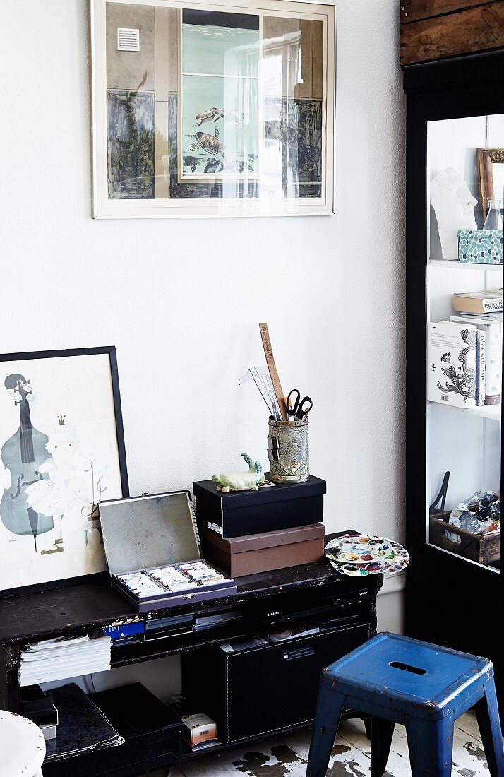 Storage boxes and drawing utensils on black, half-height shelves and blue, retro metal stool