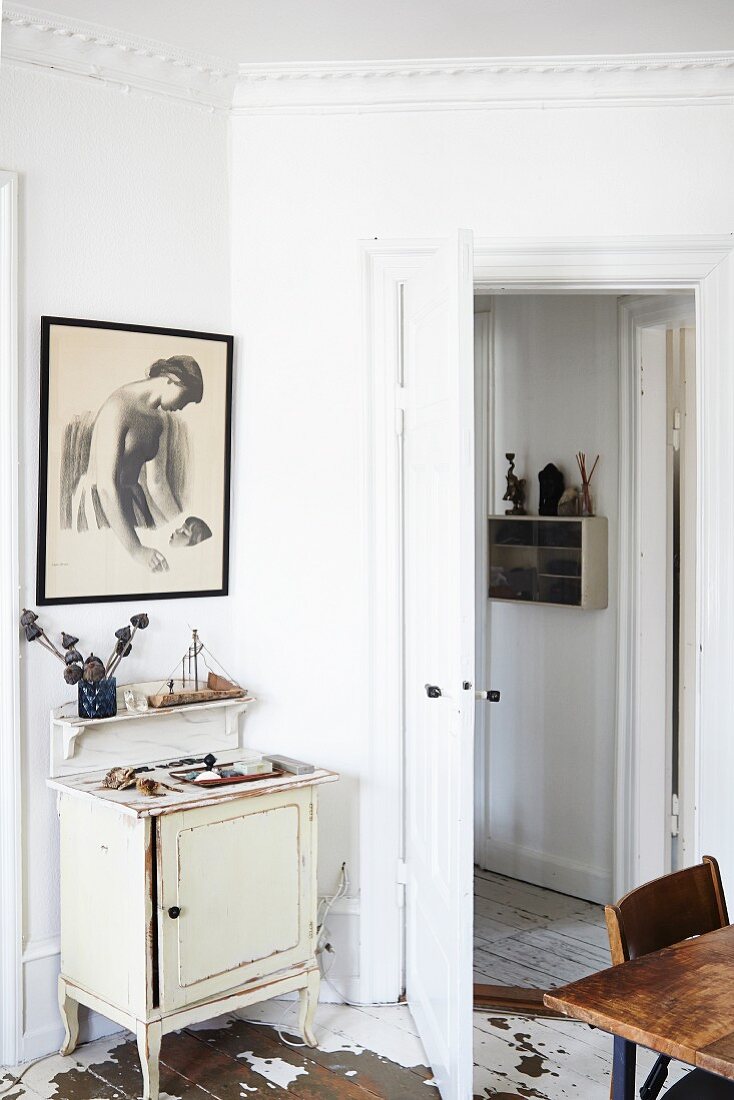Kleiner Vintage Schrank, Konsole und gerahmte Zeichnung in Zimmerecke hinter offener Tür