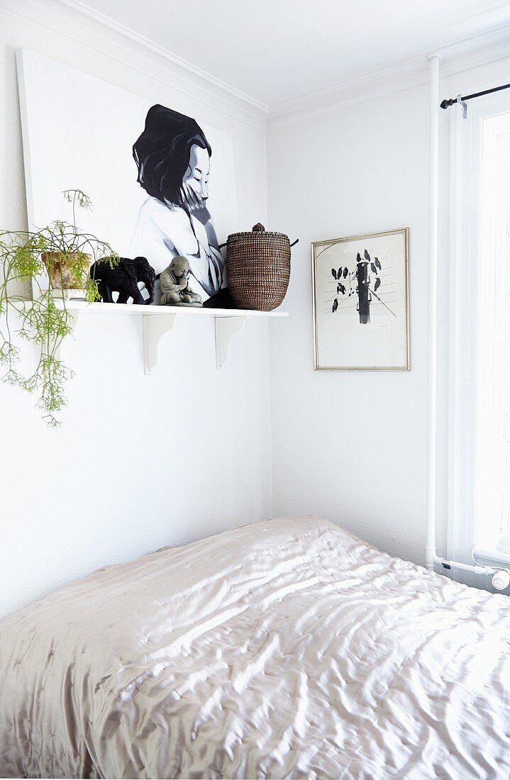 Bett mit glänzender Tagesdecke, darüber Wandkonsole mit Bild und Zimmerpflanze
