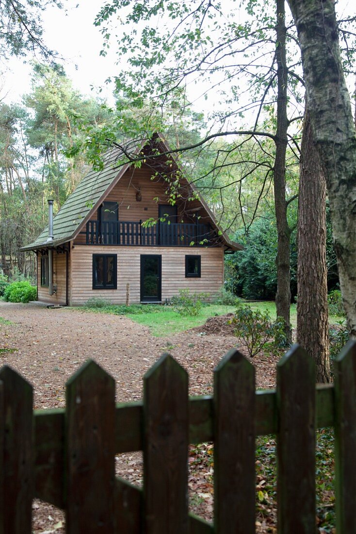 Blick über Gartenzaun auf Waldlichtung mit Zedernholz verkleidetes Holzhaus