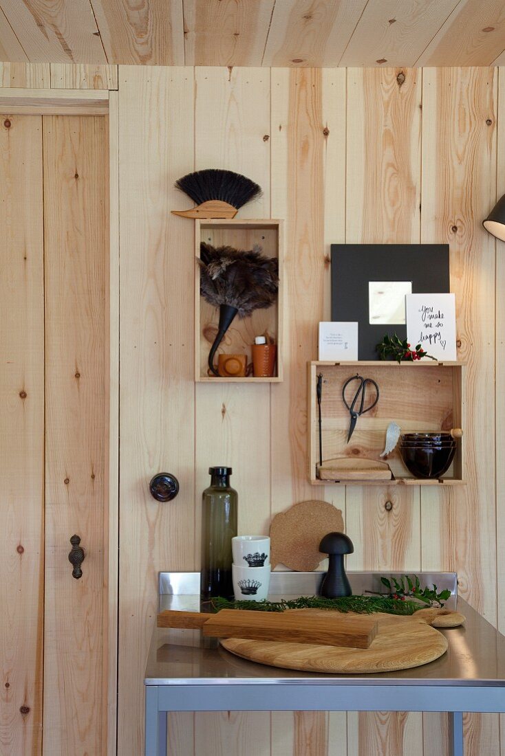 Chopping board on table with stainless steel worksurface below wooden boxes hung on pine wall