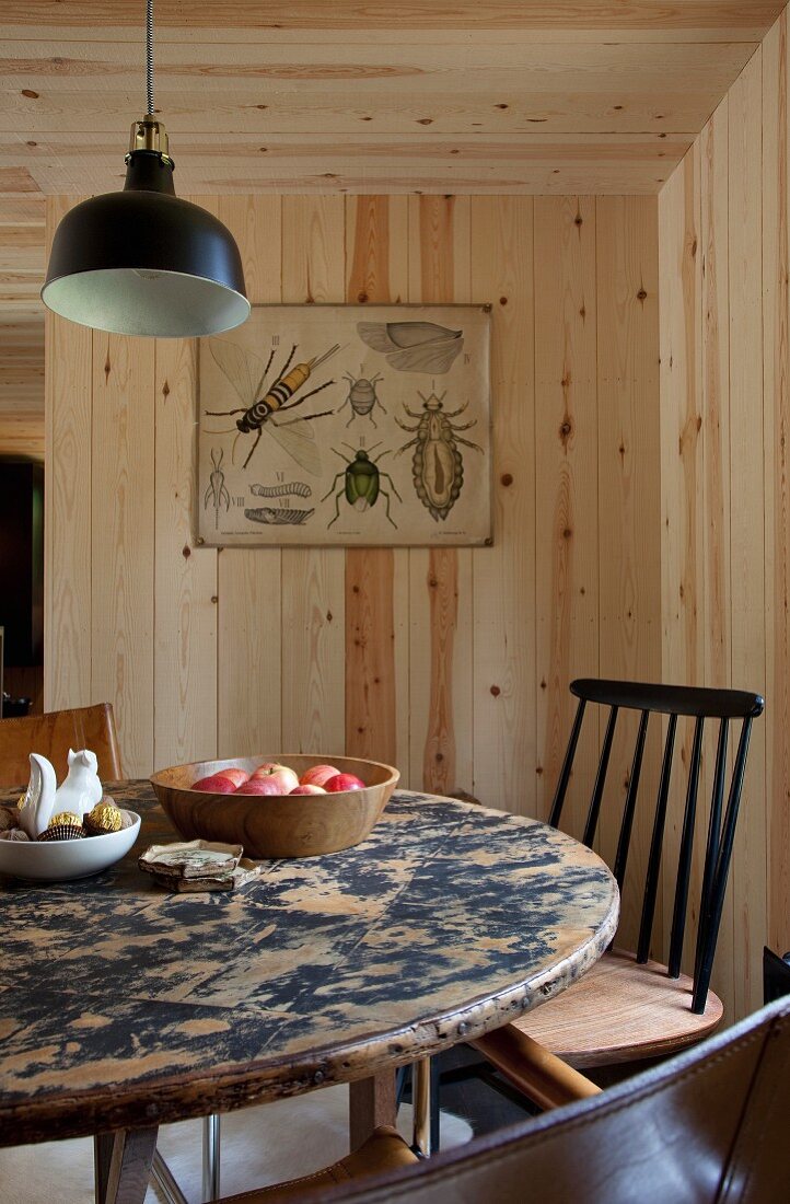 Round, vintage dining table below black pendant lamp in wood-clad room