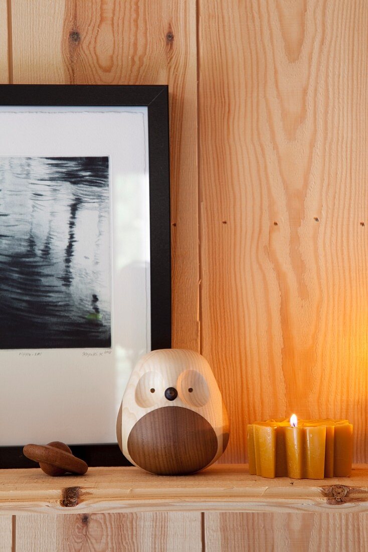 Wooden owl ornament and tealight on shelf on wooden wall