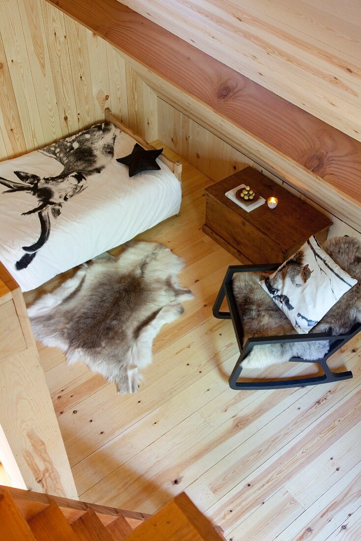 View down onto rocking chair, bed and animal-skin rug on wooden floor