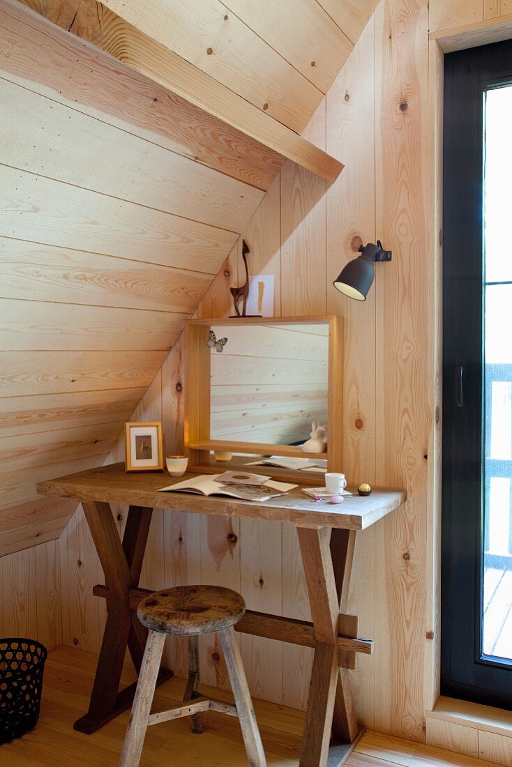 Mirror on rustic console table and stool under sloping ceiling in corner of wood-clad room