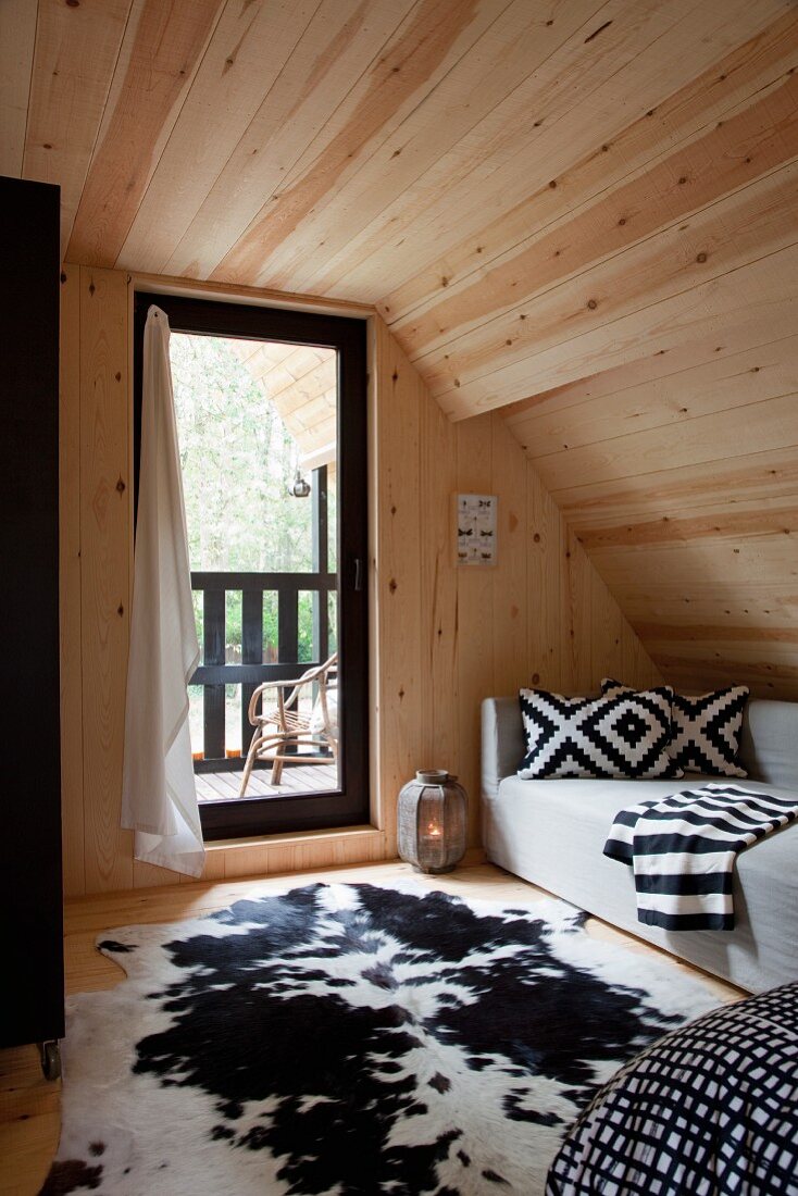 Wood-clad, cosy, attic bedroom with black and white colour scheme and view onto balcony