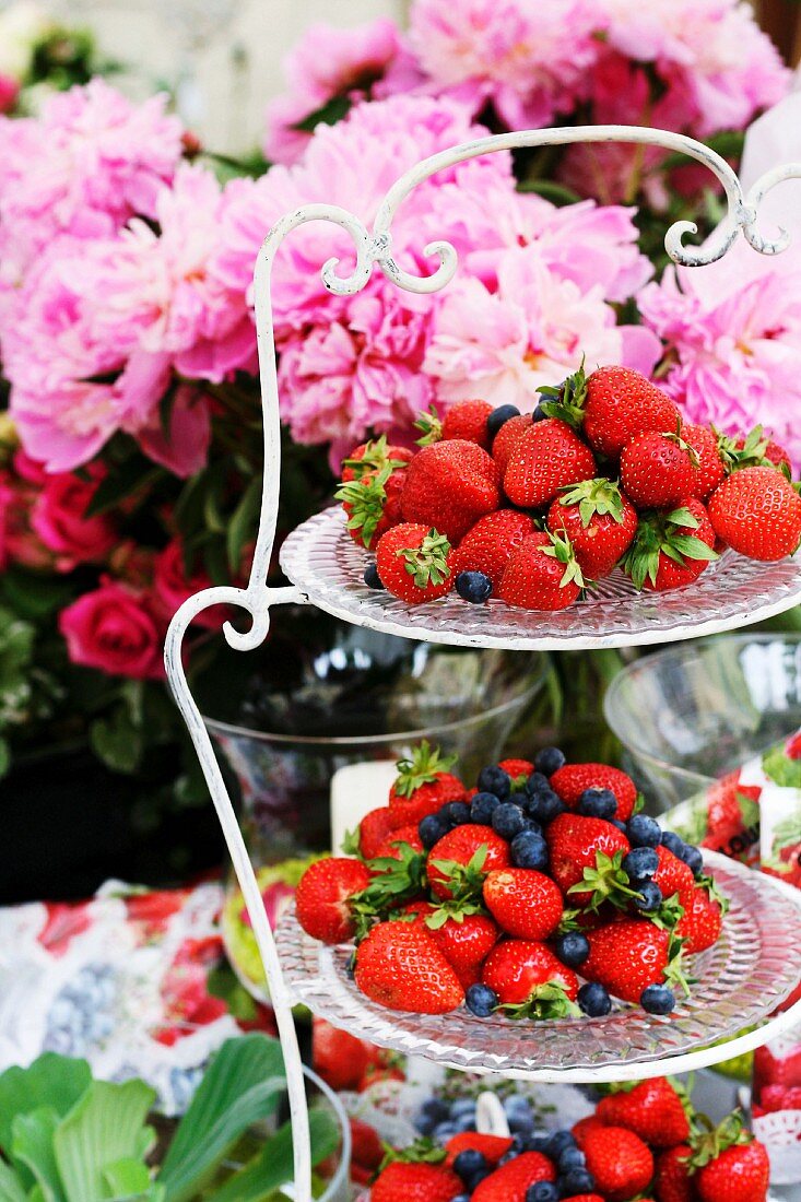 Strawberries & blueberries on cake stand in front of peonies