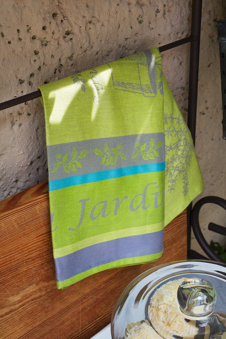 A green tea towel hanging on a metal shelf against the wall of a house