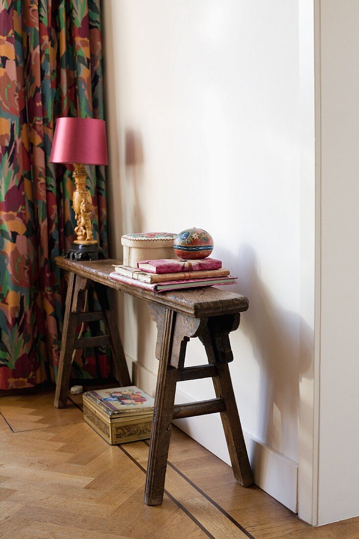 Schmale, antike Holzbank mit Tischleuchte mit pinkfarbenem Schirm, vor weisser Wand