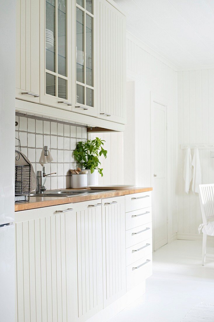 Zeile einer skandinavischen Einbauküche mit weissen profilierten Fronten und Arbeitsplatte aus Holz