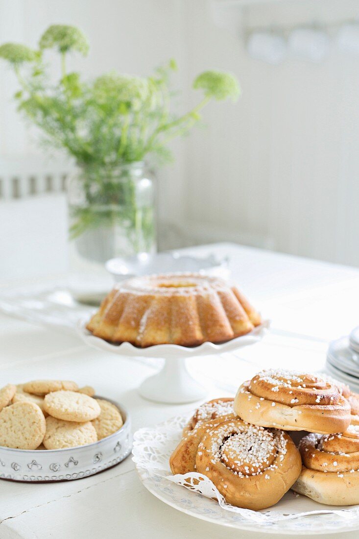 Coiled pastries, biscuits and bundt cake on table set for afternoon coffee with white tablecloth