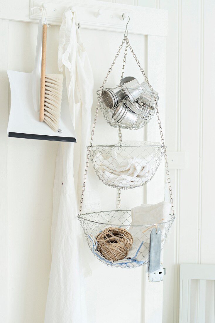 Dustpan and brush and tiered baskets suspended from peg on door in white kitchen