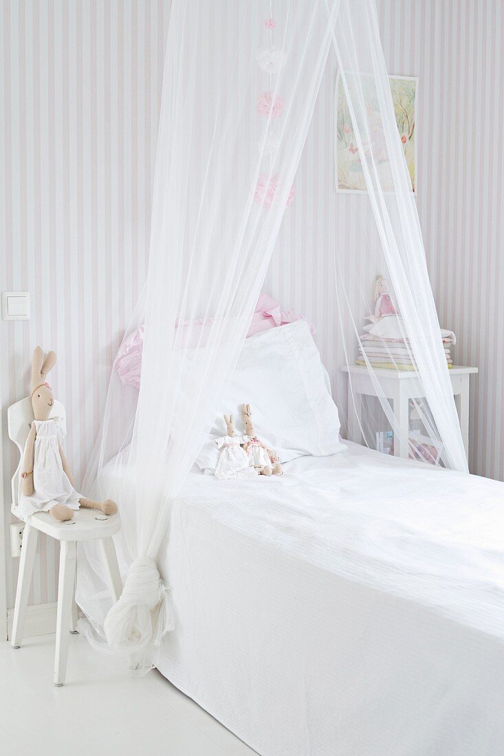 Bed with draped mosquito net and bunny soft toys leaning against pillow in child's bedroom