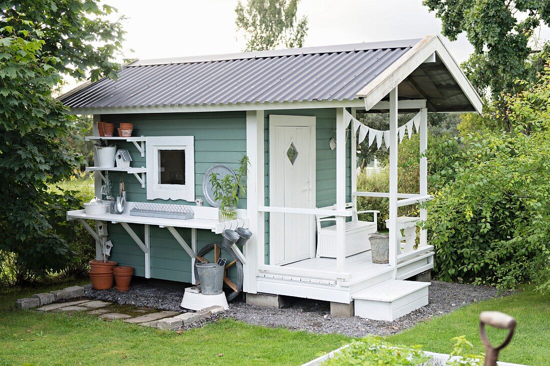 Schwedisches Gartenhaus mit Eingangsveranda, seitlich ein Arbeitstisch mit Wandborden