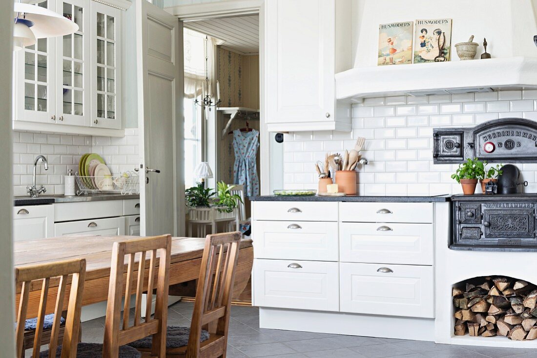 Country-house kitchen with white drawers, cast iron oven and dining area with wooden chairs around table