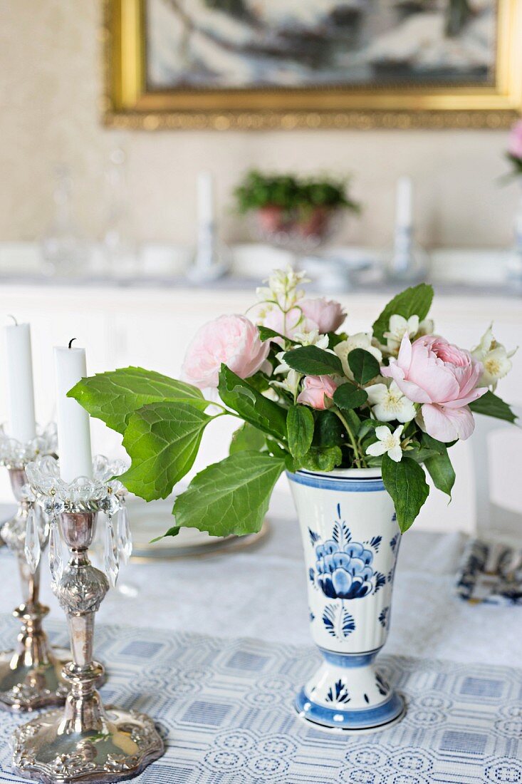 Silberne Kerzenleuchter und kleiner Blumenstrauss in weiss-blauer Vase auf Tisch