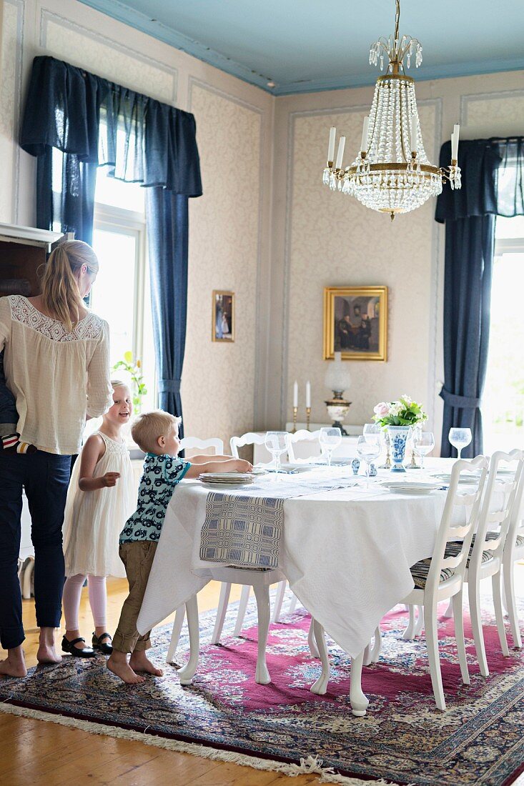 Mother and children in traditional dining room with festively set table below chandelier