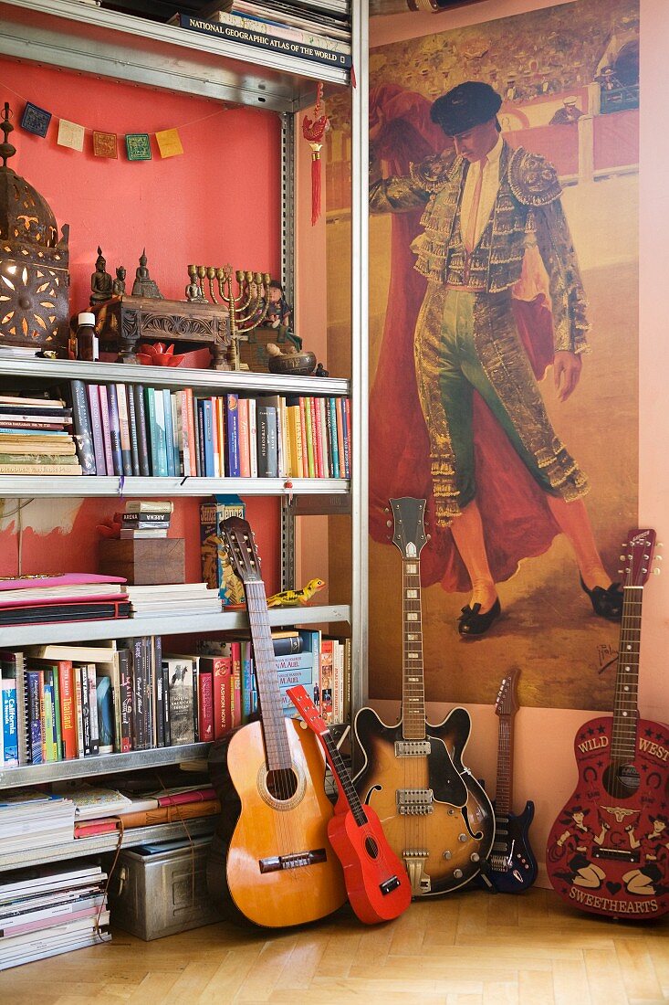 Eklektische Zimmerecke mit Torero-Poster, Gebetsregalfach, Büchern und unterschiedlichen Gitarren