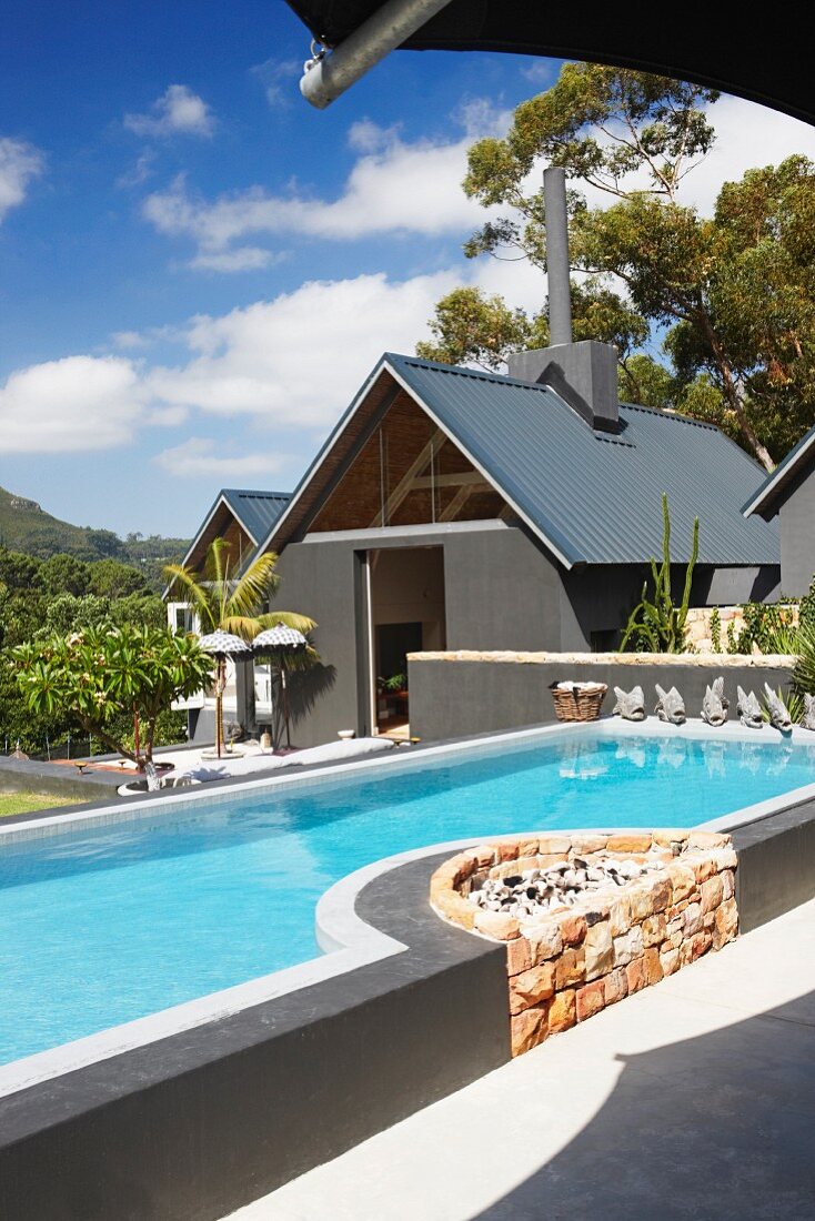 Zeitgenössischer Pool mit integriertem Grillplatz aus Natursteinen, vor Wohnhaus in tropischem Umfeld