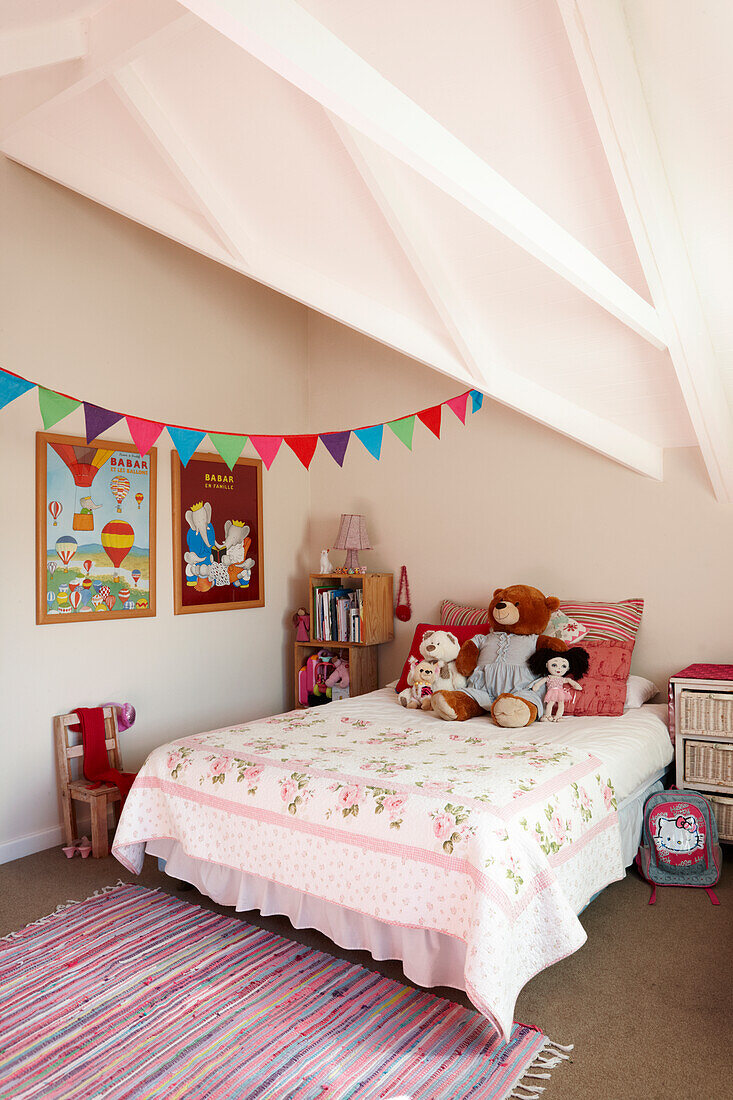 Soft toys on double bed and colourful bunting below sloping ceiling in girl's bedroom