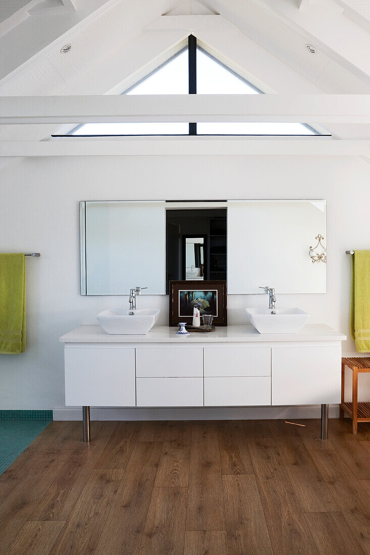 Long, modern washstand with two countertop sinks and white base unit below mirror on gable wall in attic