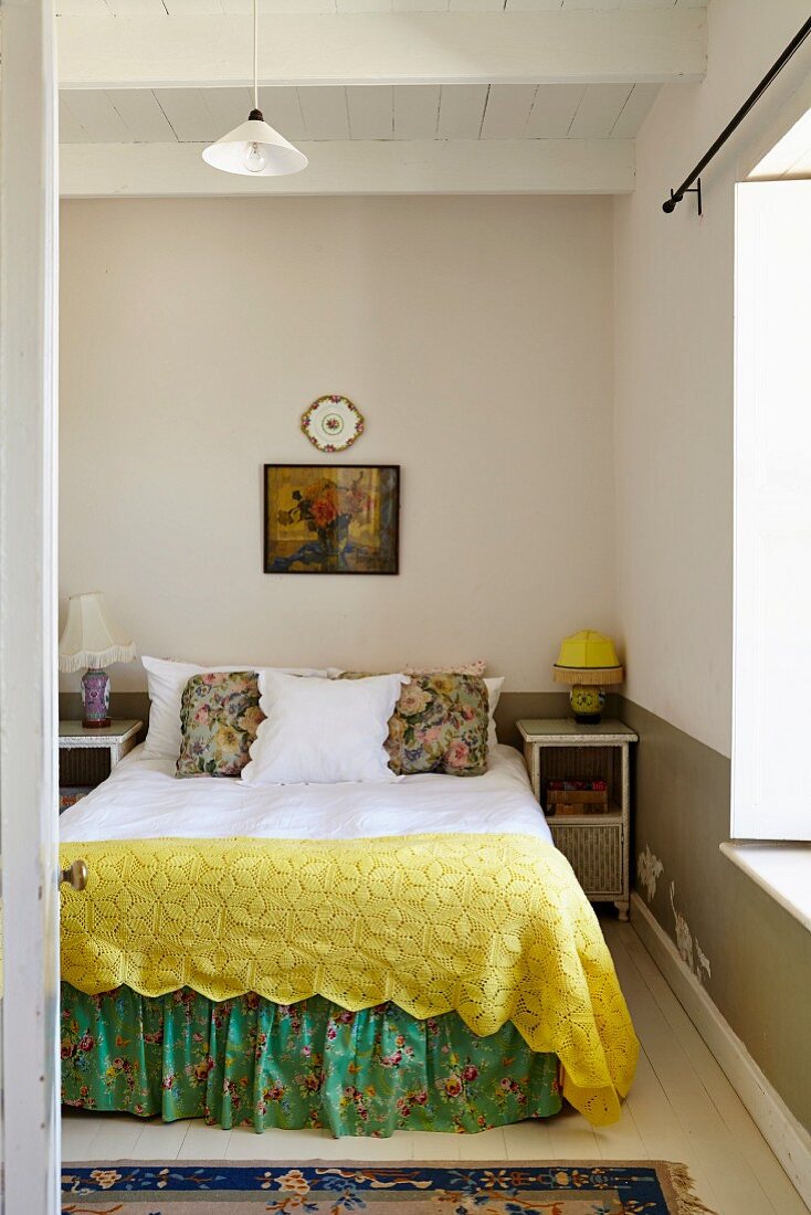 Double bed with yellow blanket and floral valance in simple bedroom