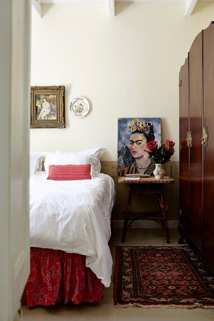 Blick ins Schlafzimmer auf Bett mit weisser Bettwäsche, seitlich Nachttisch mit Portrait einer Künstlerin, Frida Kahlo
