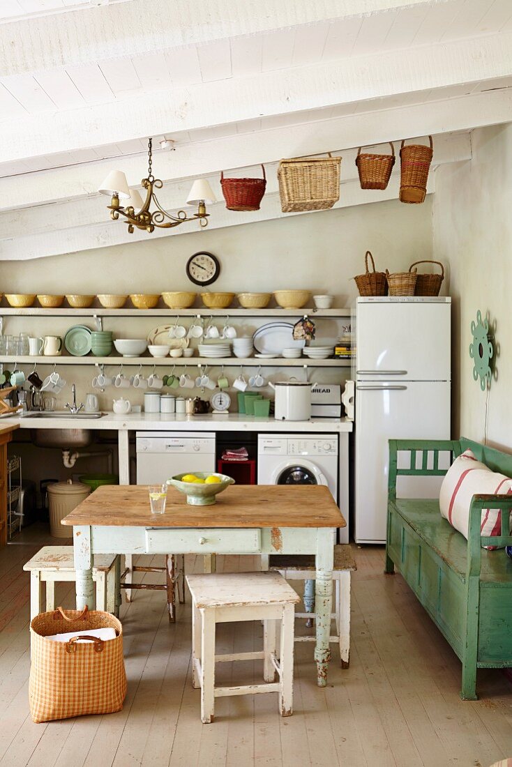 Rustikaler Tisch und Hocker, an Wand grüne Sitzbank, vor schlichter Küchenzeile in ländlicher Ambiente