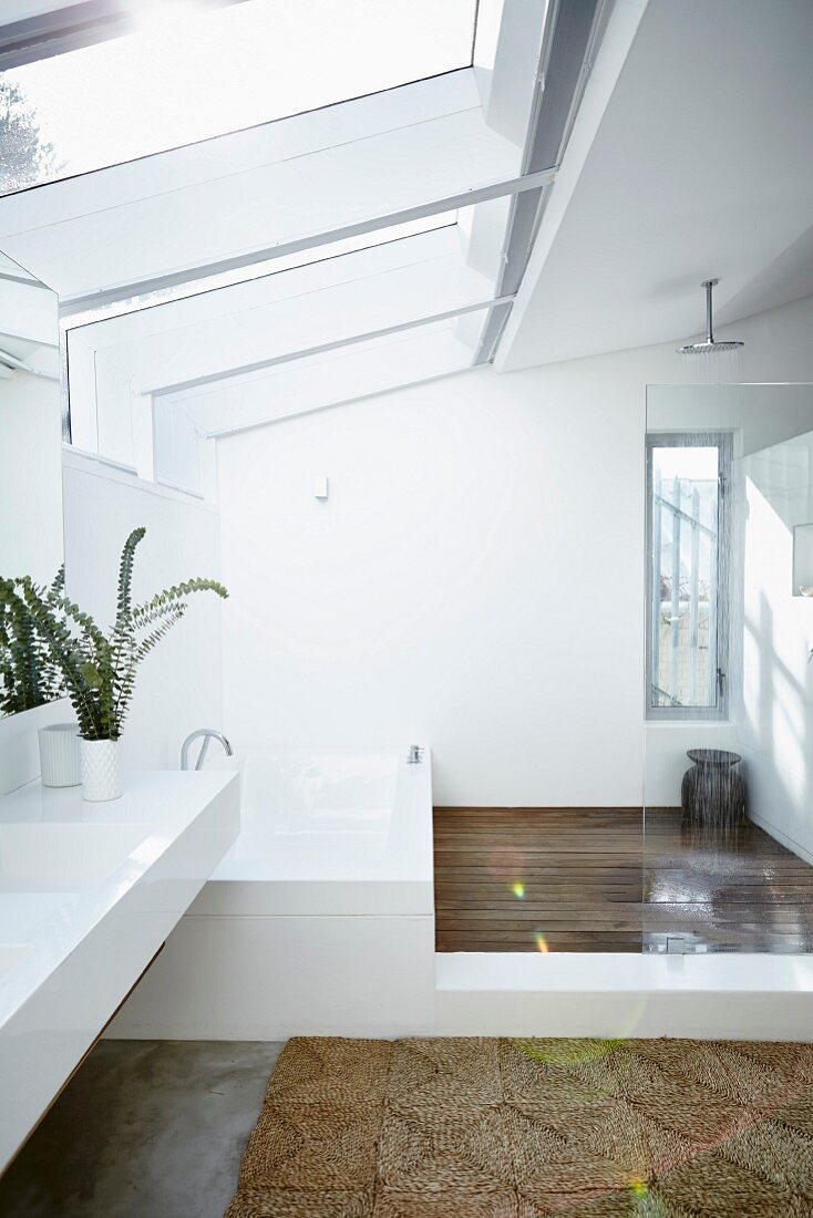 White designer bathroom; long washstand with bathtub at far end in floor-level shower area below large skylights