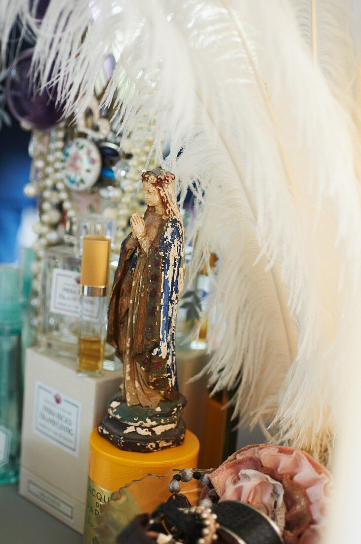 Madonna figurine amongst perfume bottles and white feathers