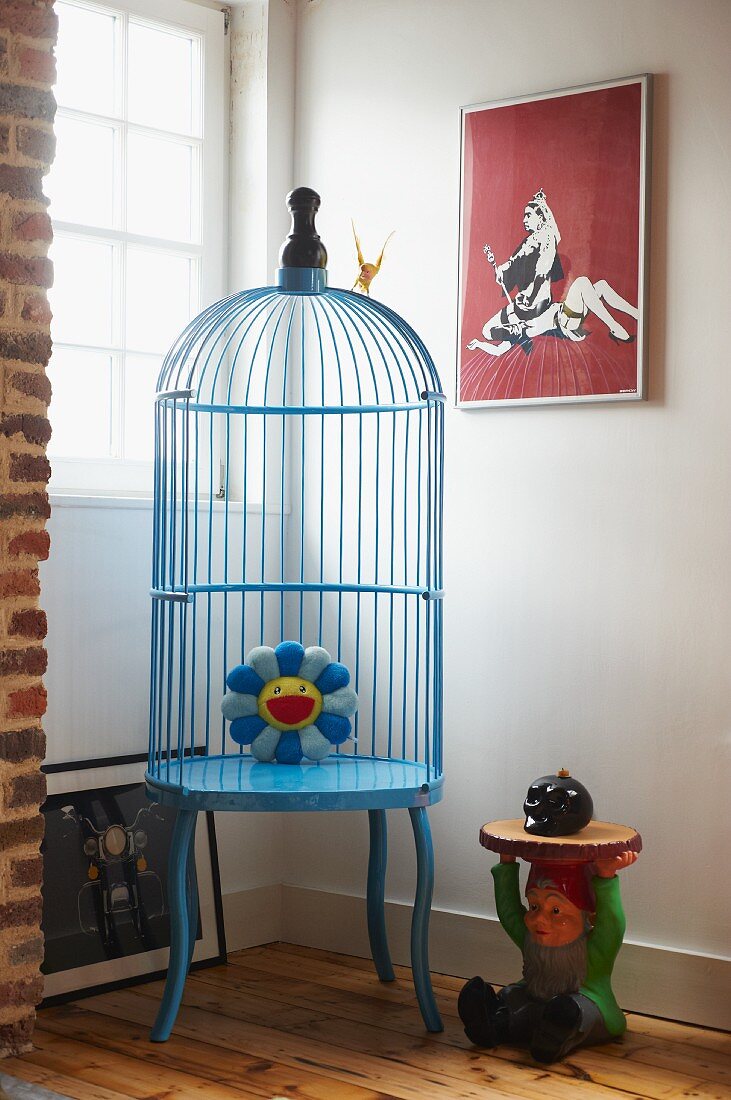 Pale blue, retro birdcage next to garden gnome and window in corner