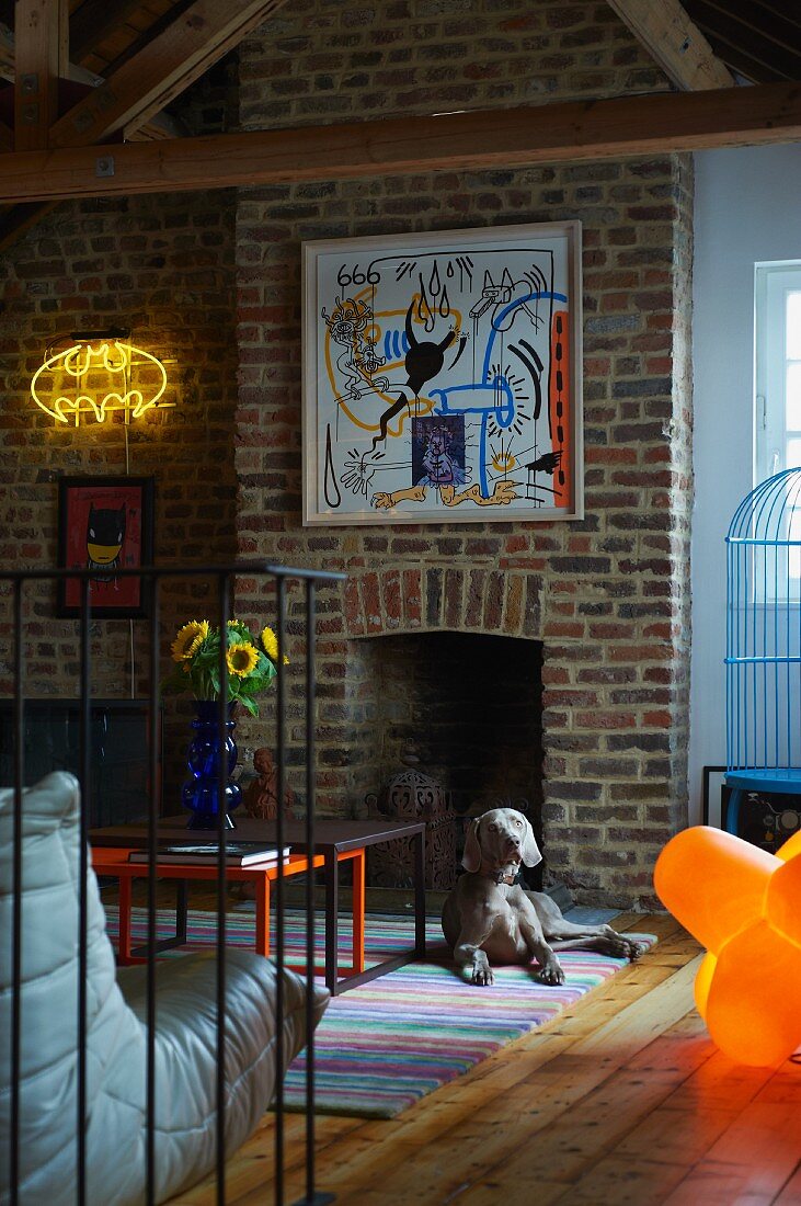 Artworks on brick wall and dog lying on floor in front of open fireplace in brick wall