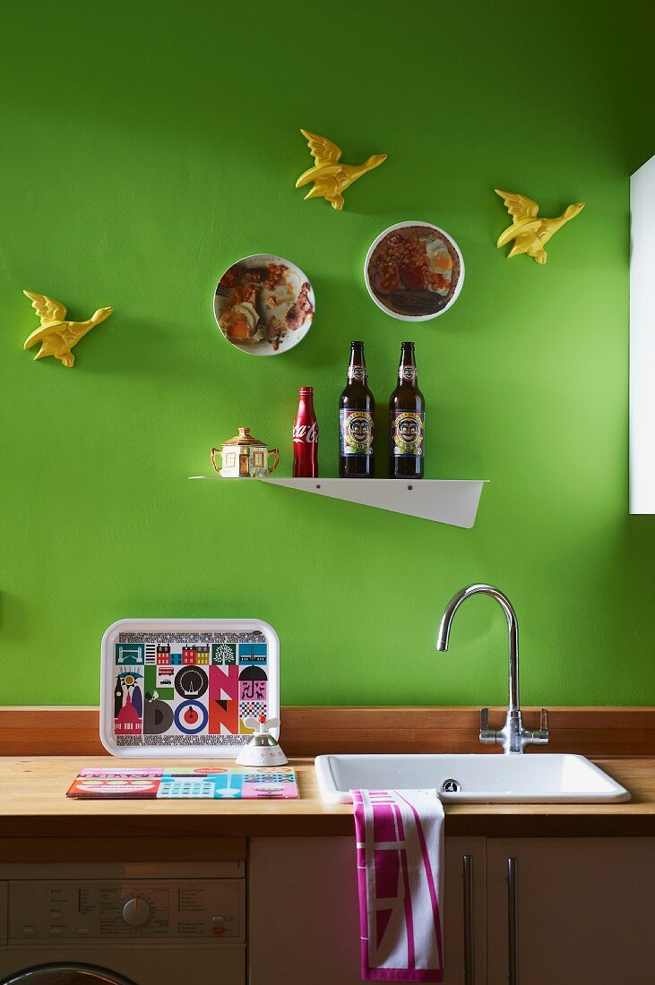 Minimalistische Küchenzeile mit Holz Arbeitsplatte, Metallregal zwischen Entenfiguren an grüner Wand